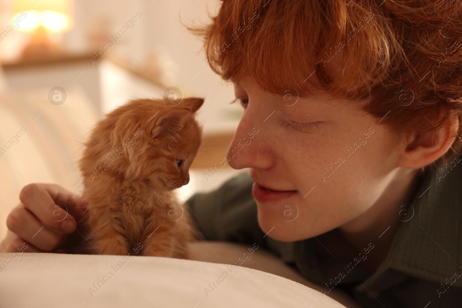 Photo of Redhead teenage boy with cute ginger kitten on sofa indoors