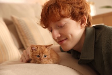 Photo of Redhead teenage boy with cute ginger kitten on sofa indoors