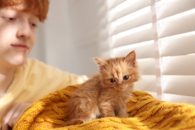 Photo of Redhead teenage boy with cute ginger kitten indoors, selective focus