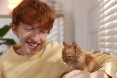 Photo of Redhead teenage boy with cute ginger kitten indoors, selective focus