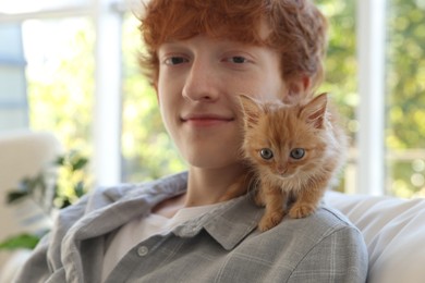 Photo of Redhead teenage boy with cute ginger kitten indoors