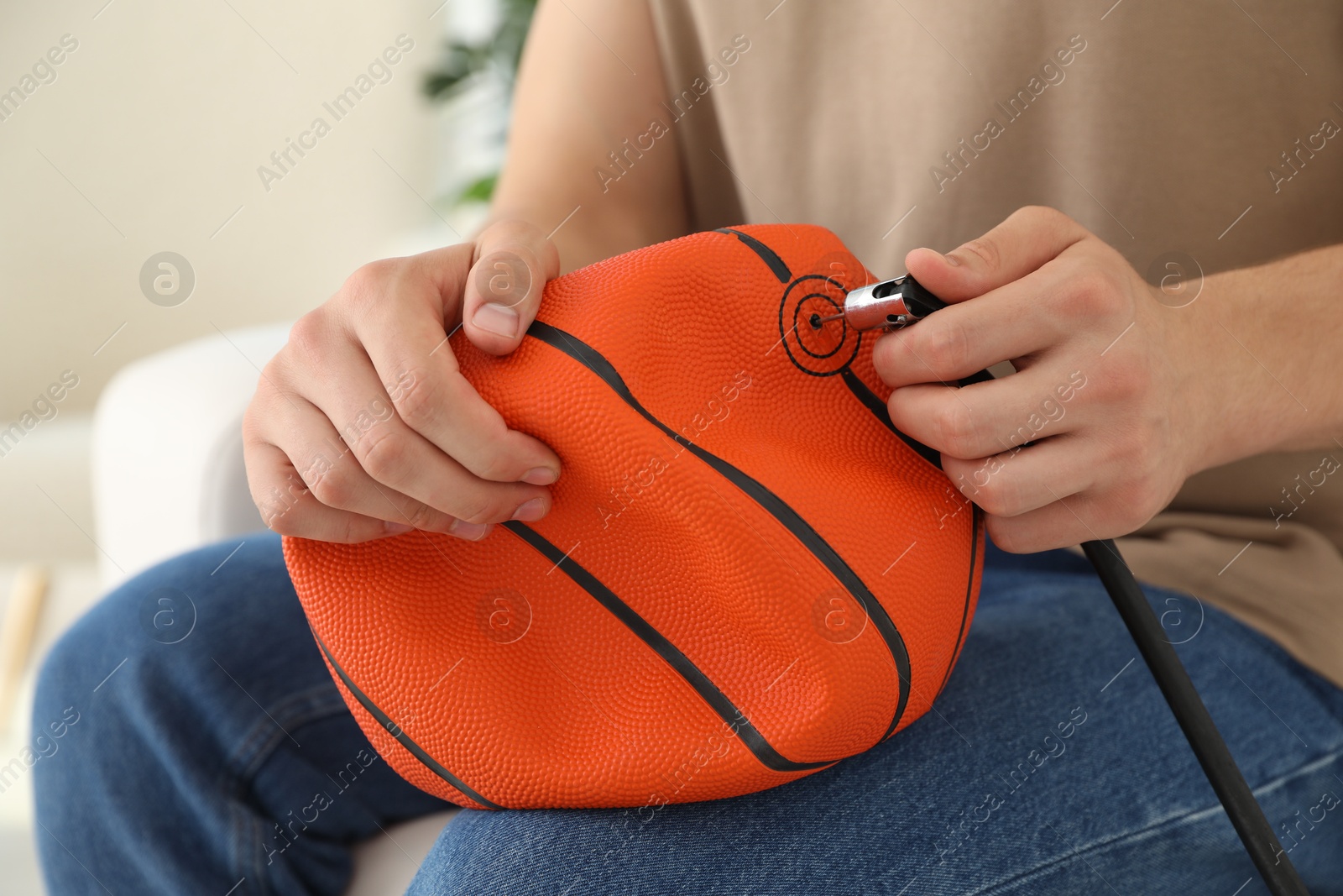 Photo of Man inflating basketball ball with air compressor indoors, closeup