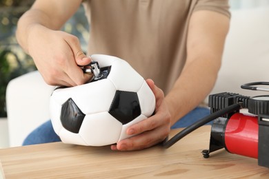 Photo of Man inflating soccer ball with air compressor indoors, closeup