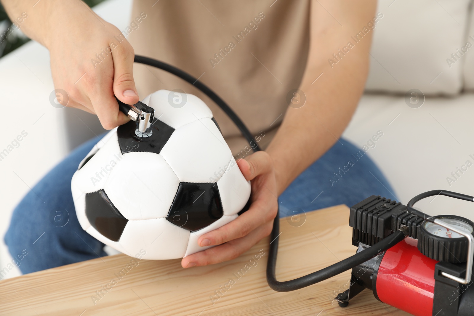 Photo of Man inflating soccer ball with air compressor indoors, closeup