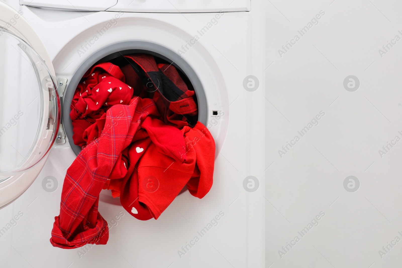 Photo of Washing machine with laundry near light wall, closeup. Space for text