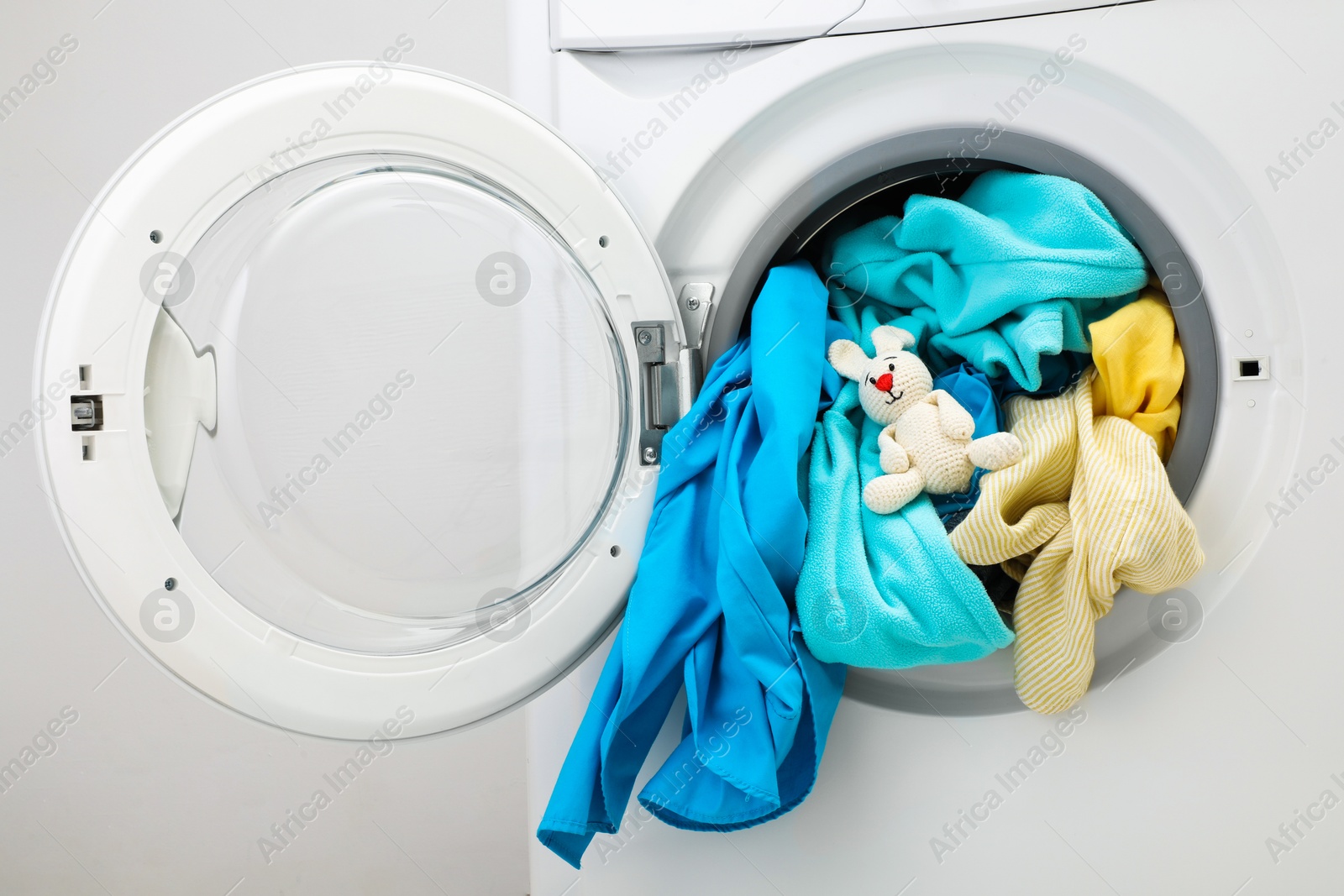 Photo of Washing machine with clothes and toy bunny near light wall, closeup