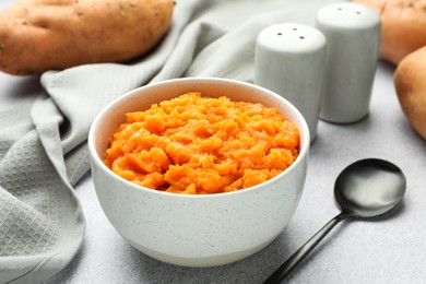 Photo of Tasty mashed sweet potato in bowl, spoon and fresh vegetables on gray table, closeup