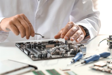 Photo of Man installing computer chip onto motherboard at white table, closeup