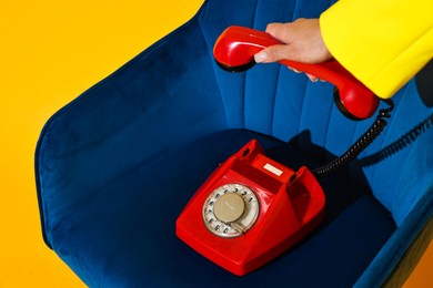 Photo of Woman with red corded telephone on blue armchair against yellow background, closeup