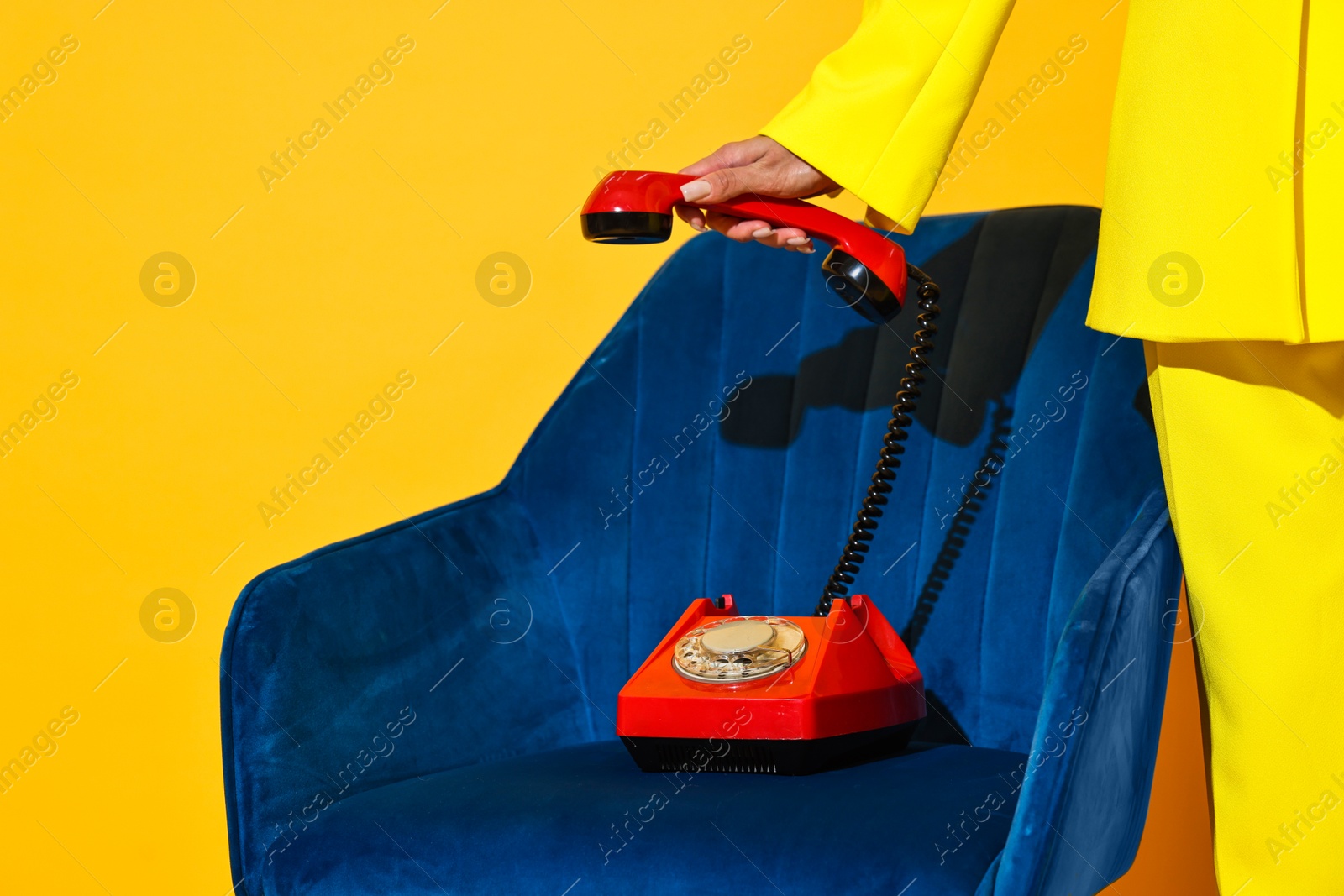 Photo of Woman with red corded telephone on blue armchair against yellow background, closeup