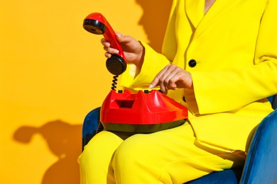 Photo of Woman with red corded telephone on blue armchair against yellow background, closeup