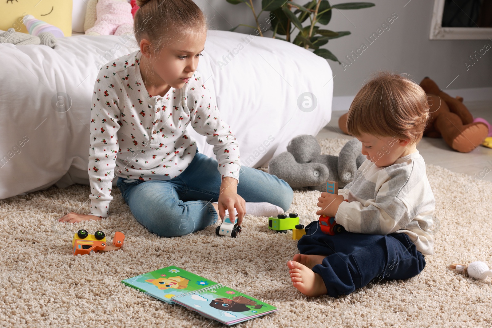 Photo of Sister and brother playing with toy cars on floor indoors