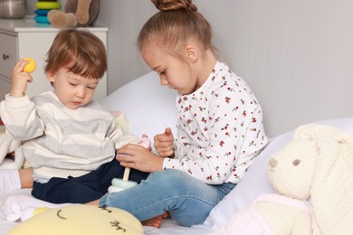 Photo of Sister and brother playing with toy pyramid on bed indoors