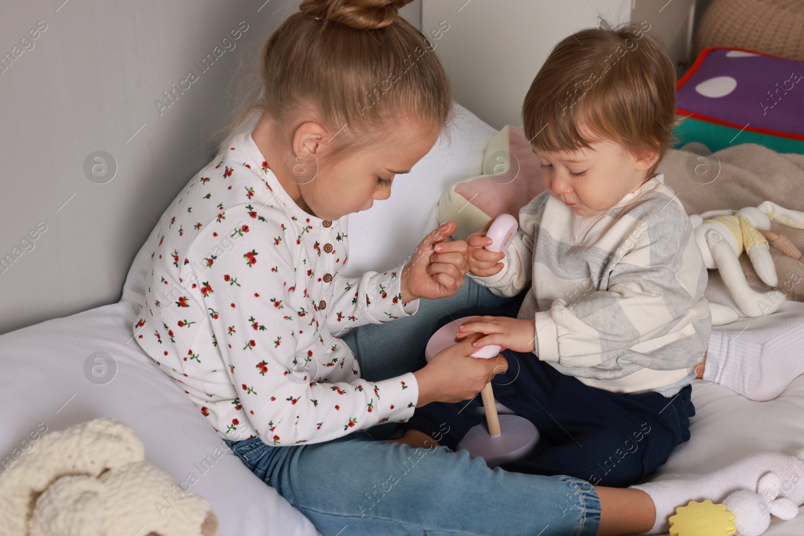 Photo of Sister and brother playing with toy pyramid on bed indoors