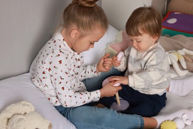 Photo of Sister and brother playing with toy pyramid on bed indoors