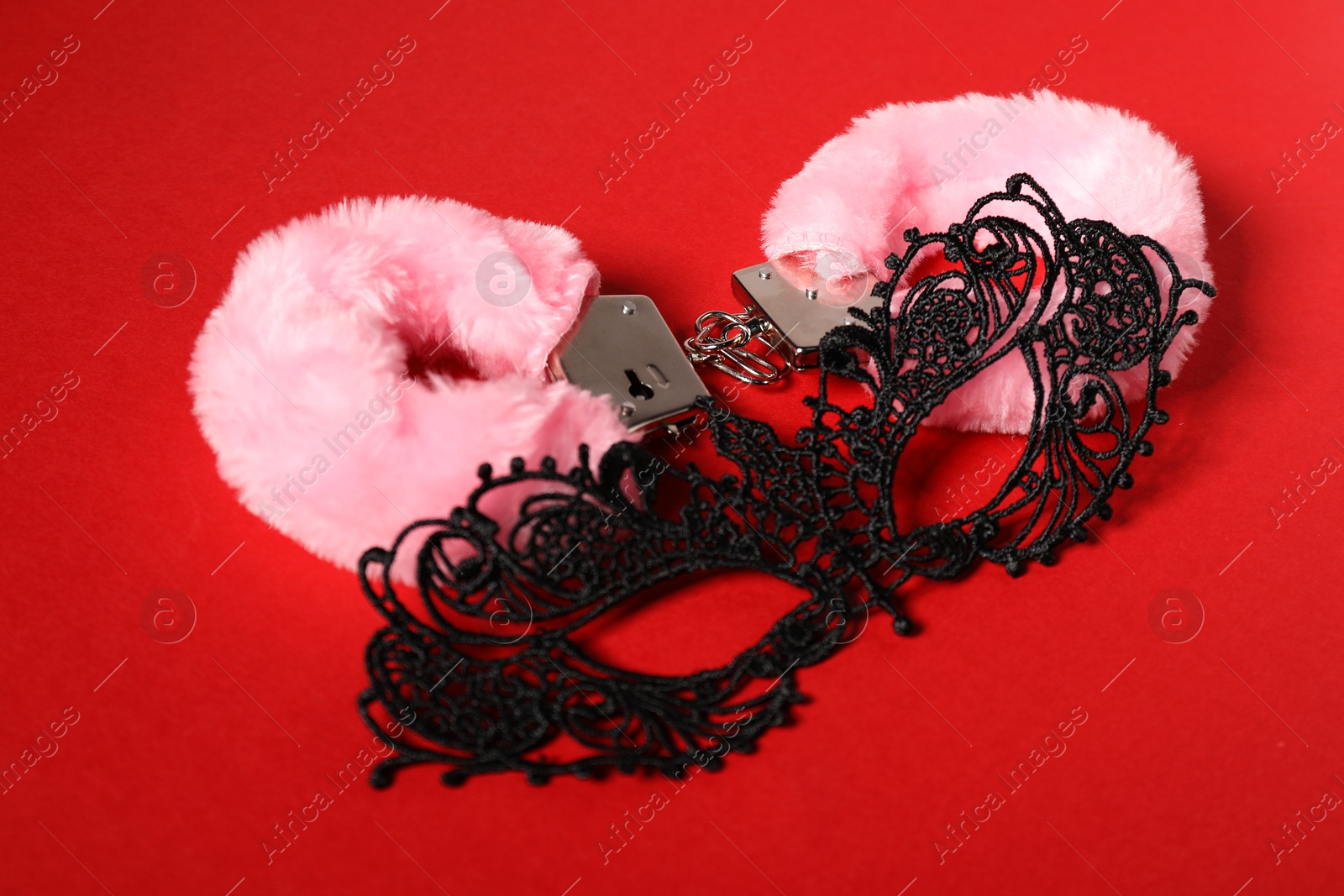 Photo of Pink fluffy handcuffs and lace mask on red background