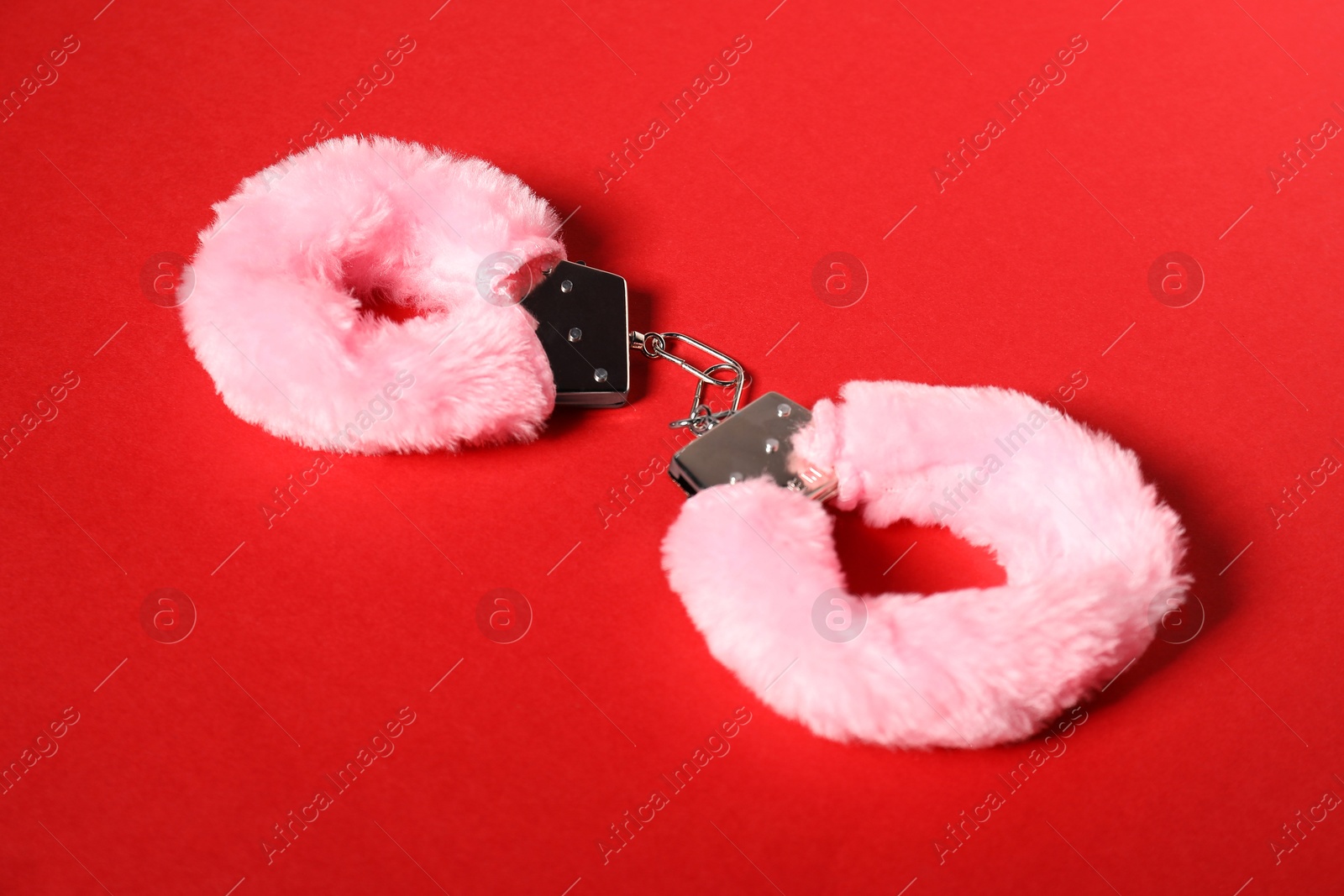 Photo of Pink fluffy handcuffs on red background. Sex toy