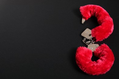 Photo of Bright fluffy handcuffs on black background, space for text