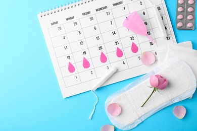 Photo of Flat lay composition with calendar and menstrual products on light blue background