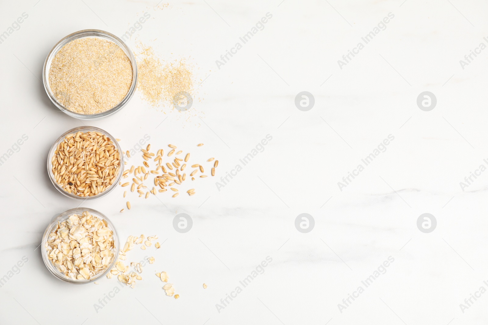 Photo of Oat bran, grains and flakes in bowls on white marble table, flat lay. Space for text