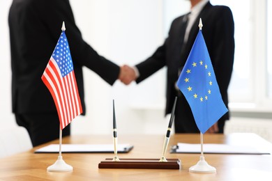 Photo of Diplomats shaking hands during meeting indoors, focus on flags of USA and European Union