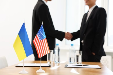 Photo of Diplomats shaking hands during meeting indoors, focus on flags of USA and Ukraine