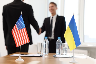 Photo of Diplomats shaking hands during meeting indoors, focus on flags of USA and Ukraine