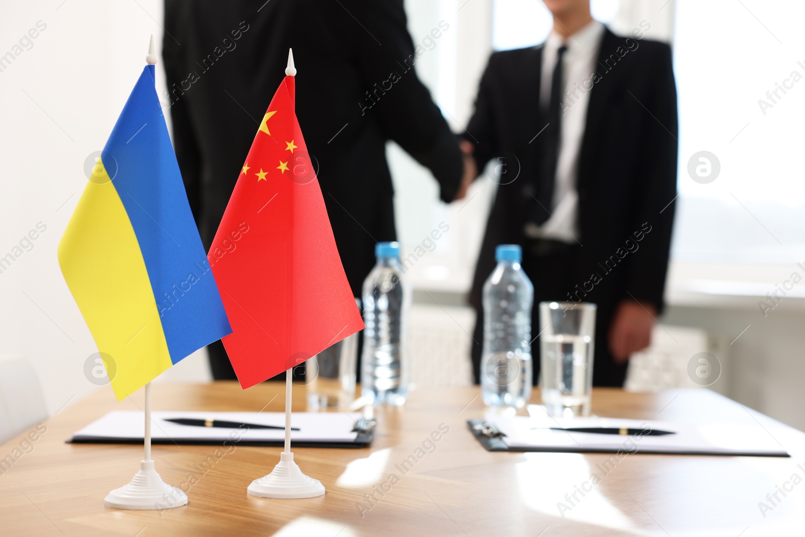 Photo of Diplomats shaking hands during meeting indoors, focus on flags of Ukraine and China