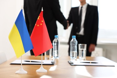 Photo of Diplomats shaking hands during meeting indoors, focus on flags of Ukraine and China