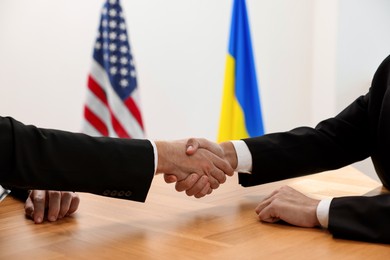 Photo of Diplomats shaking hands during meeting at wooden table indoors, closeup