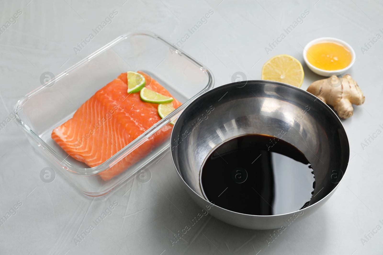 Photo of Soy sauce in bowl, salmon fillet with lime slices, honey and ginger on gray textured table, closeup