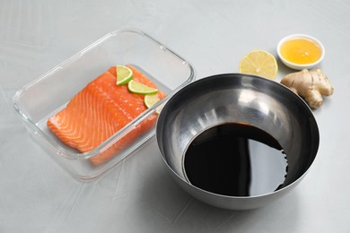 Photo of Soy sauce in bowl, salmon fillet with lime slices, honey and ginger on gray textured table, closeup