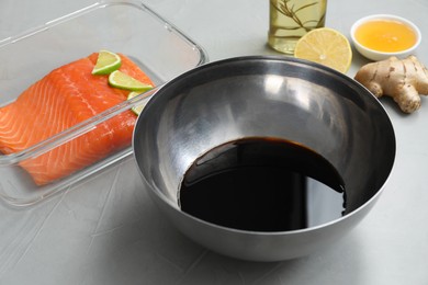 Photo of Soy sauce in bowl, salmon fillet, oil, honey, lemon and ginger on gray textured table, closeup