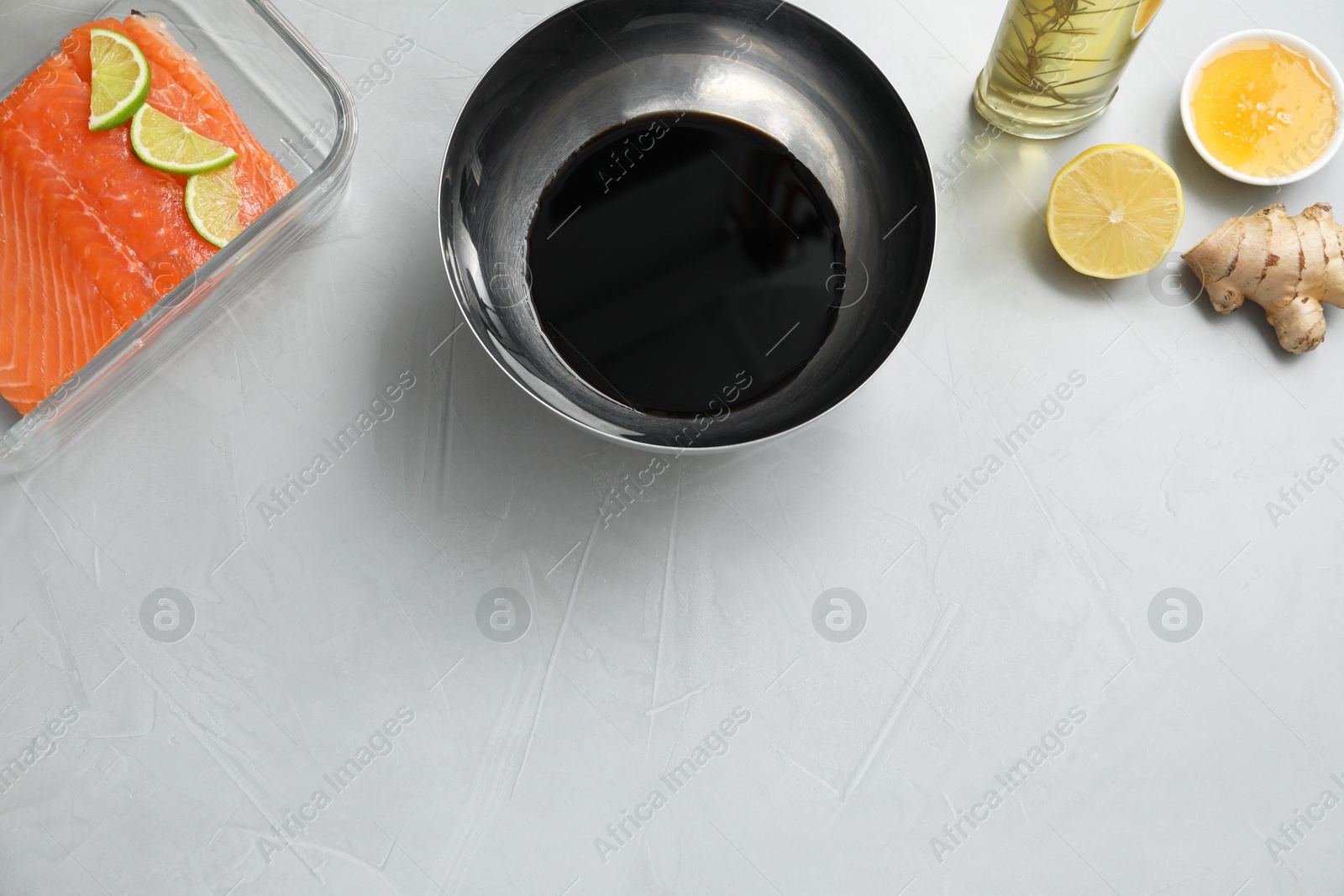 Photo of Soy sauce in bowl, salmon fillet, oil, honey, lemon and ginger on gray textured table, flat lay. Space for text