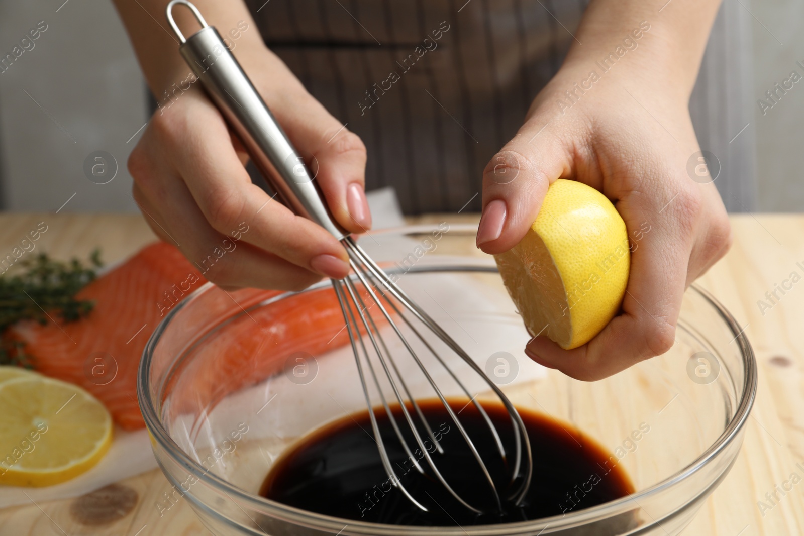 Photo of Woman squeezing lemon juice into bowl with soy sauce at table, closeup