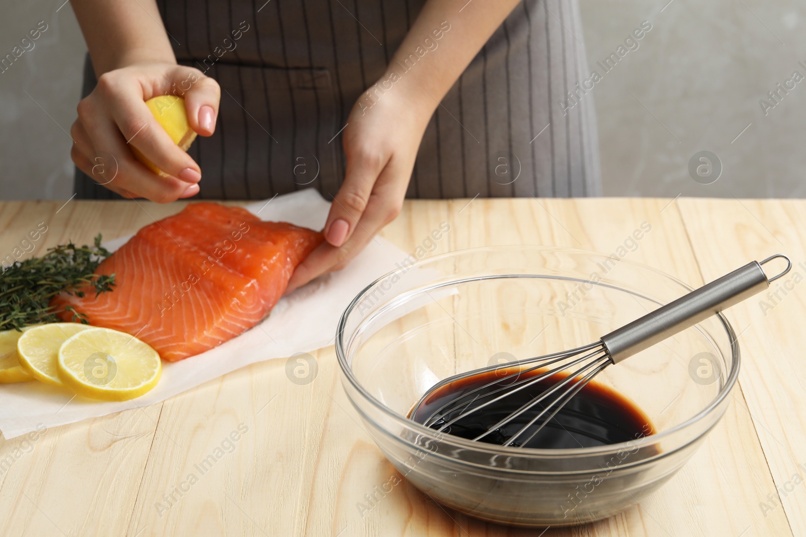 Photo of Woman squeezing lemon juice onto salmon fillet wooden at table, closeup