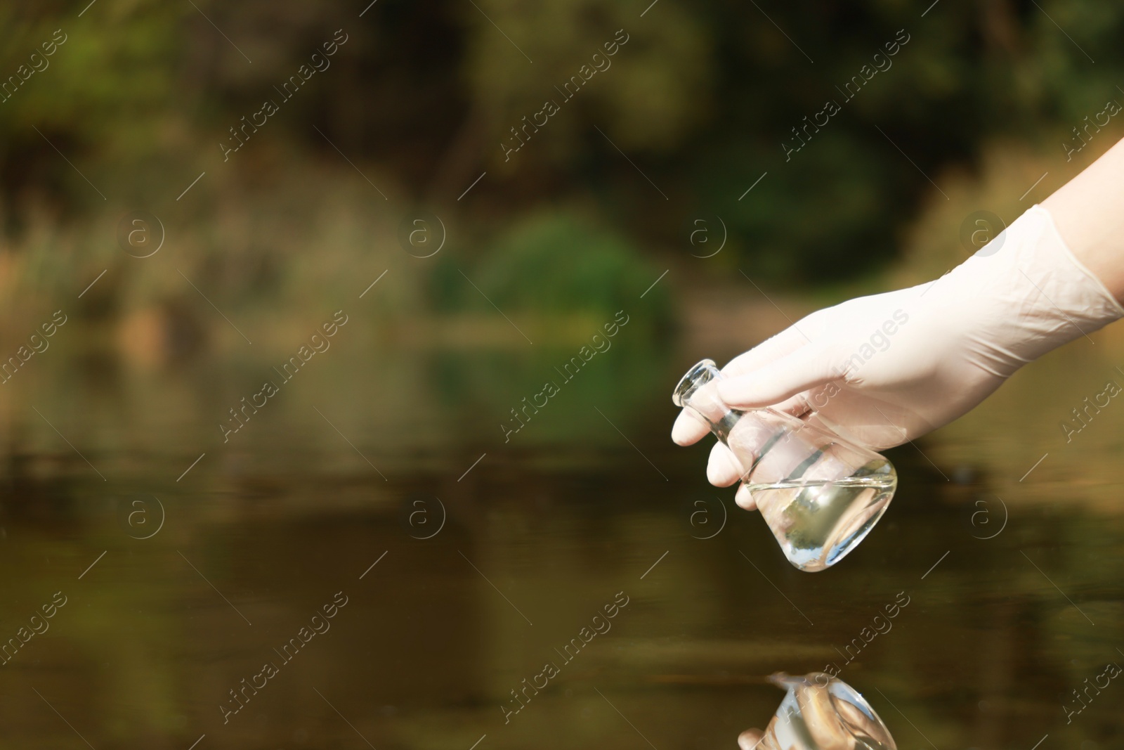 Photo of Examination of water quality. Researcher holding flask with sample from lake outdoors, closeup. Space for text