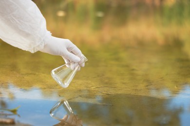 Photo of Examination of water quality. Researcher taking water sample from lake outdoors, closeup. Space for text