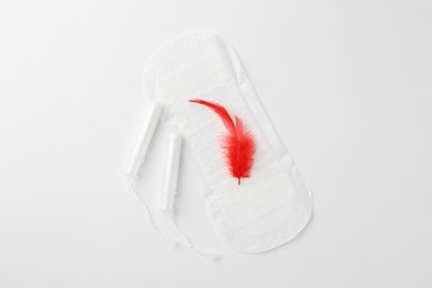 Photo of Menstrual pad with red feather and tampons on white background, top view