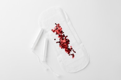 Photo of Menstrual pad with red sequins and tampons on white background, top view