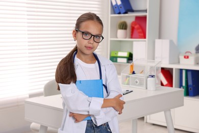 Photo of Girl with stethoscope and book pretending to be doctor indoors