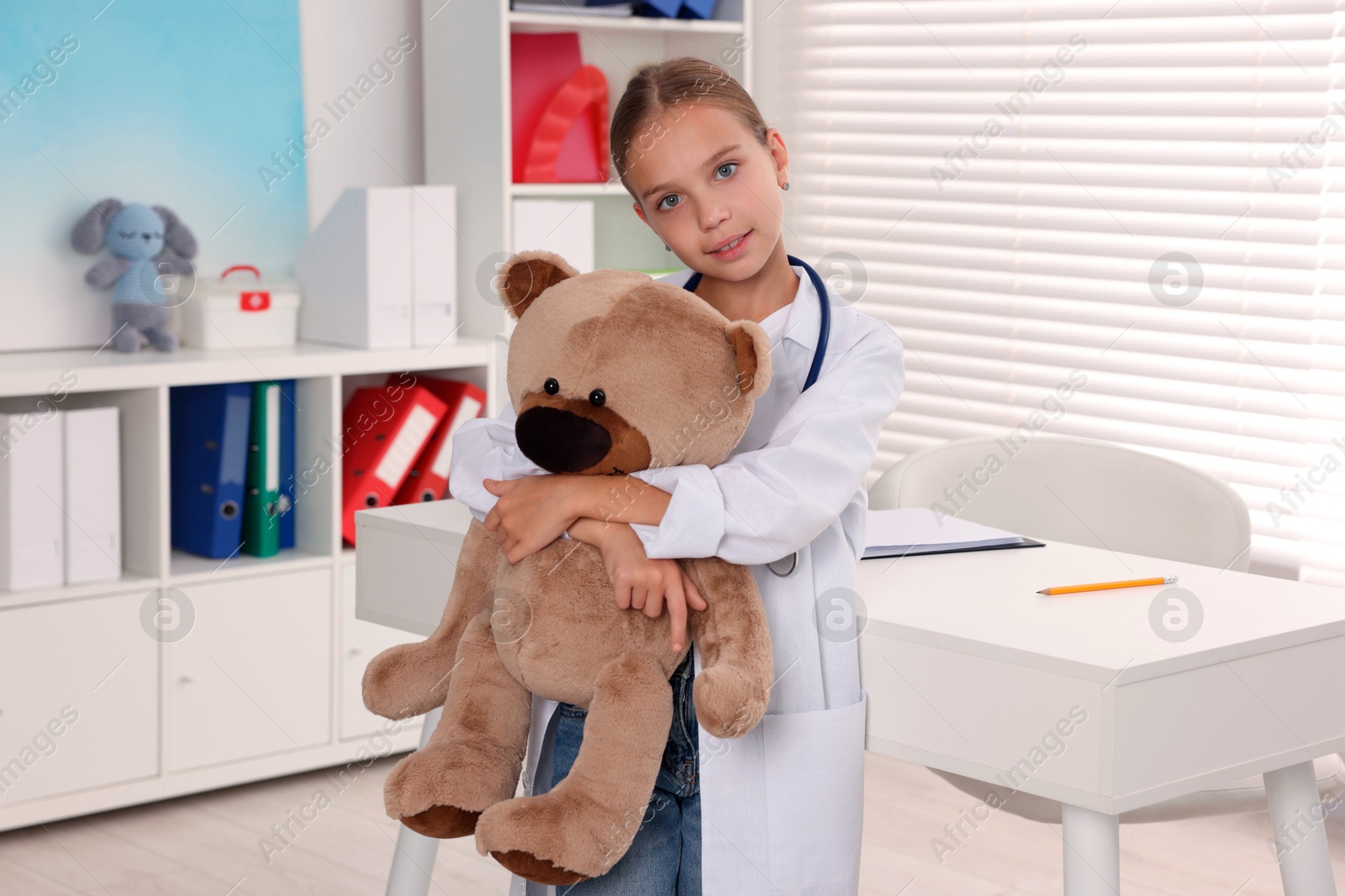 Photo of Girl with stethoscope and toy pretending to be doctor indoors