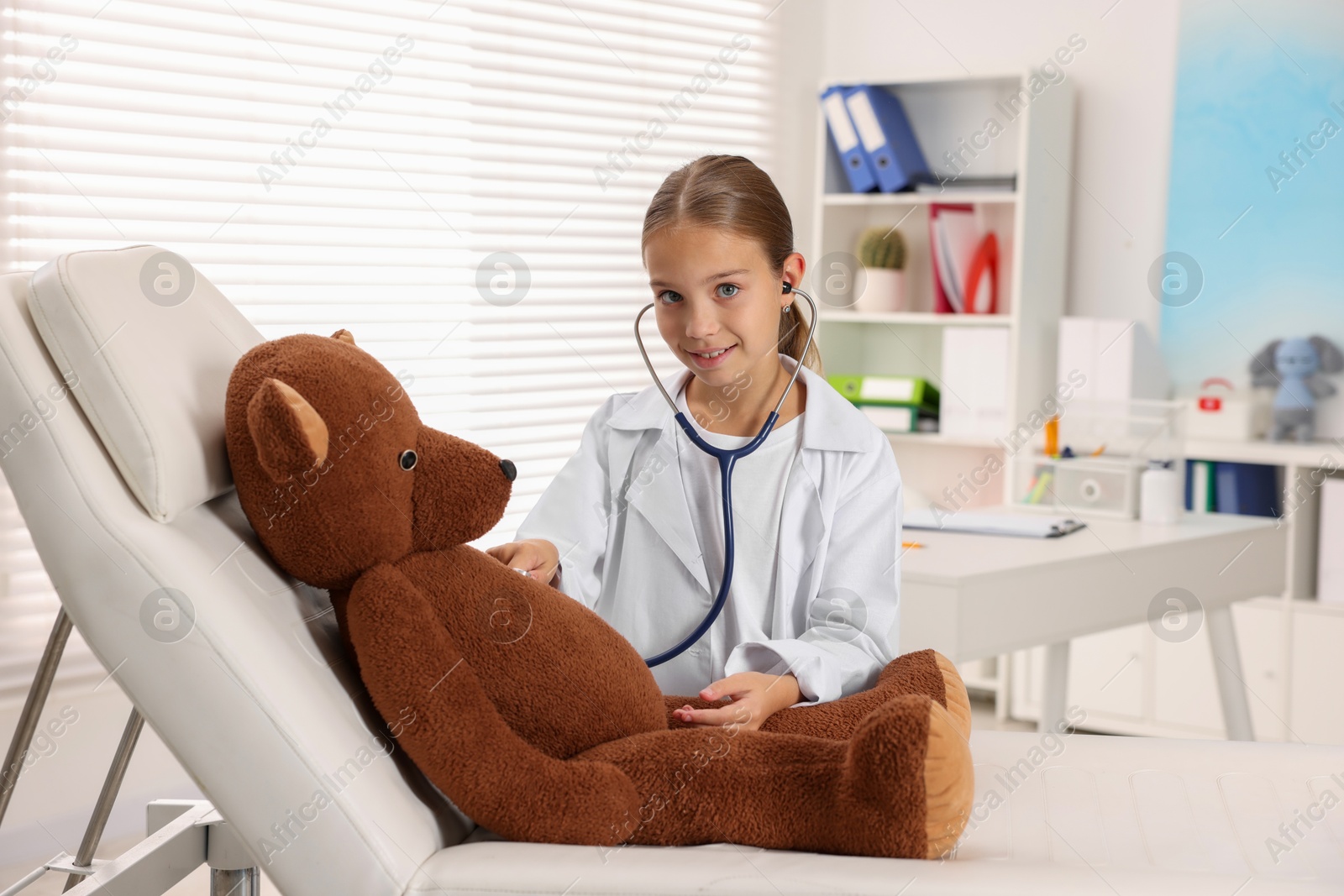 Photo of Girl with stethoscope and toy pretending to be doctor indoors