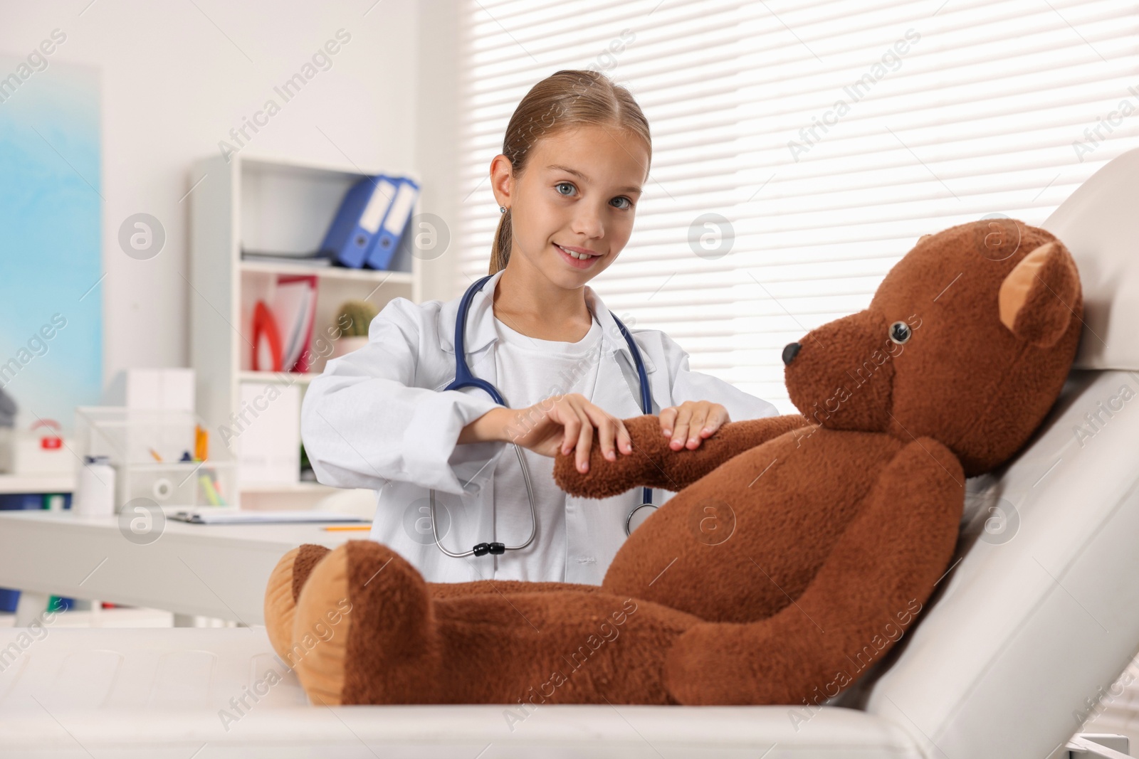 Photo of Girl with stethoscope and toy pretending to be doctor indoors