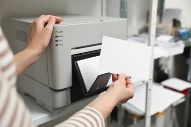 Photo of Woman with photo paper using modern printer indoors, closeup. Printing house