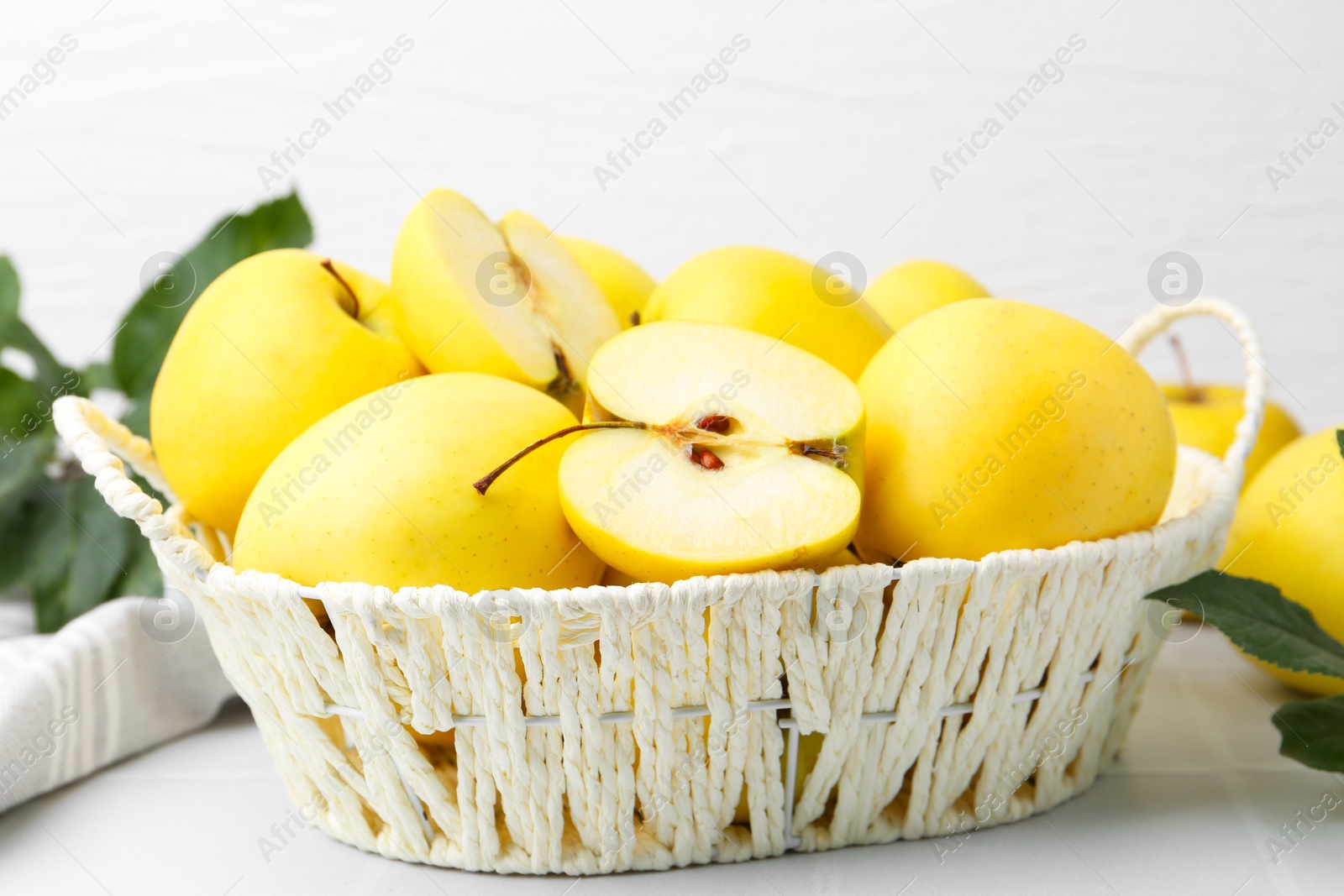 Photo of Fresh ripe yellow apples in basket on white tiled table, closeup