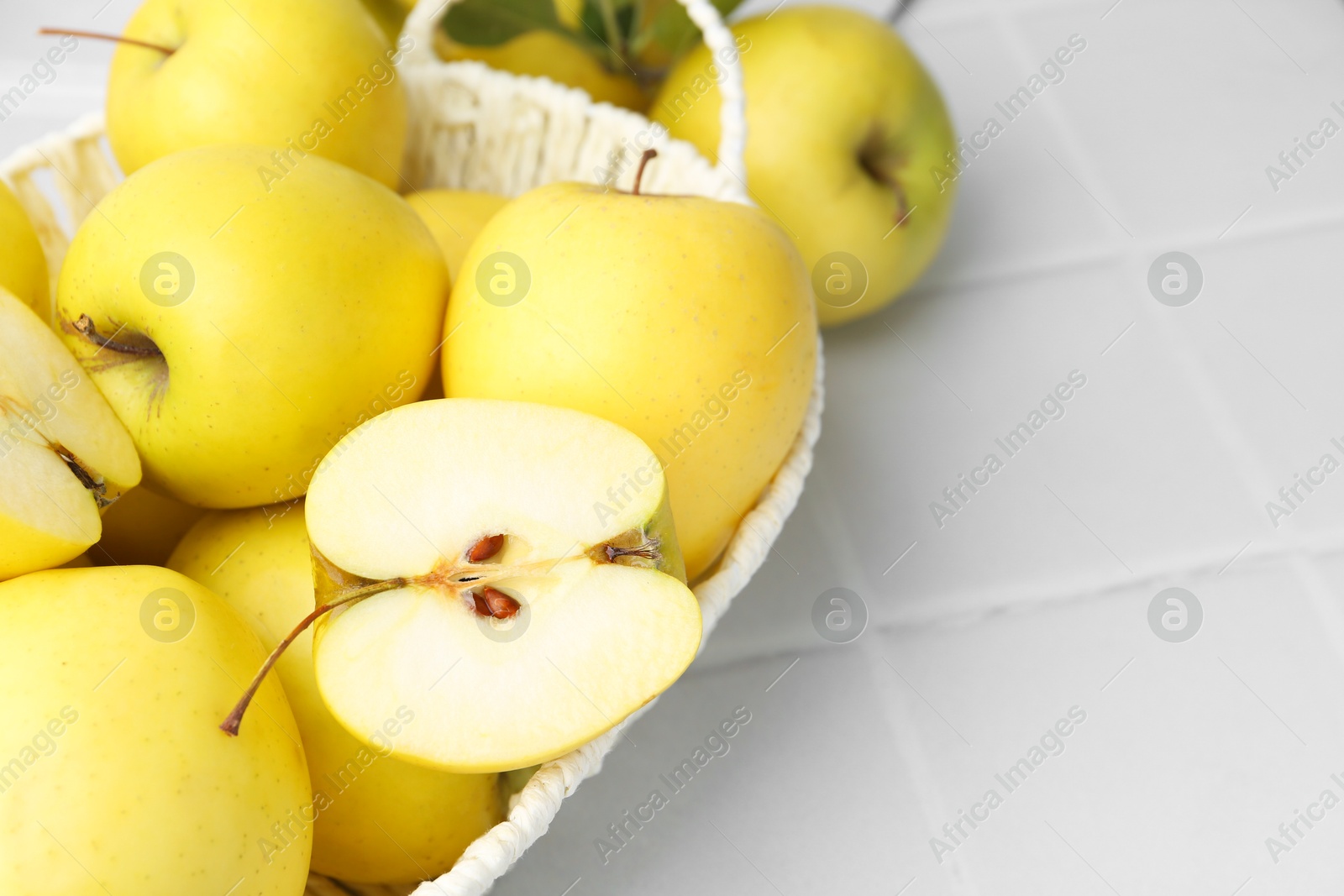 Photo of Fresh ripe yellow apples in basket on white tiled table, closeup. Space for text