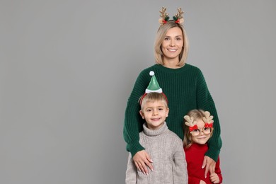 Photo of Mom with her little children in sweaters and Christmas accessories on grey background