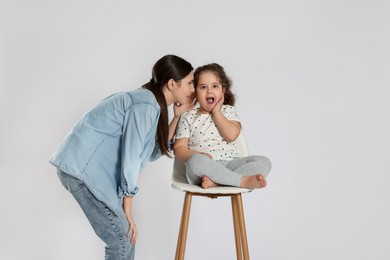 Photo of Teenage girl whispering secret to her cute little sister on white background