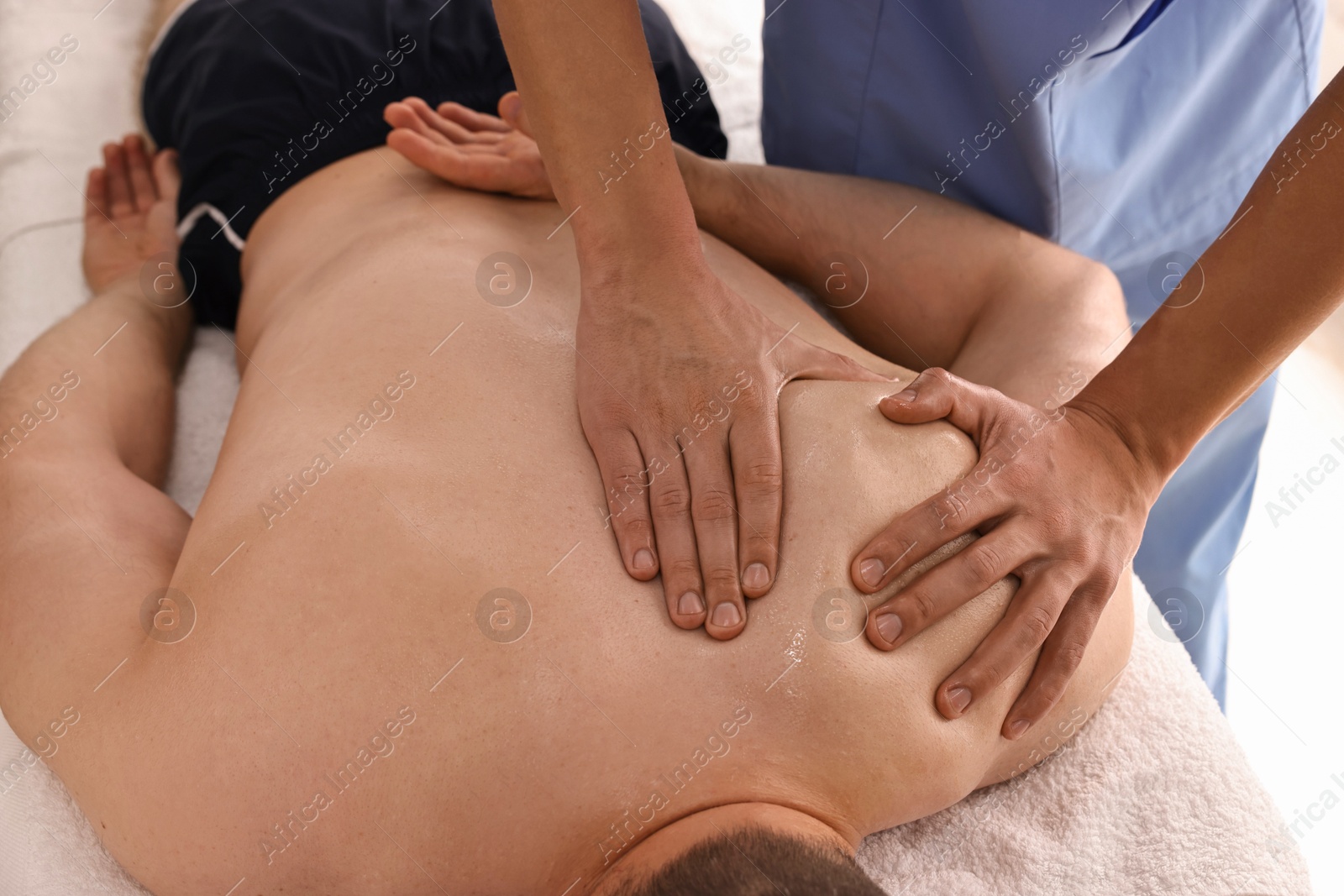 Photo of Professional physiotherapist doing shoulder massage for his client indoors, closeup